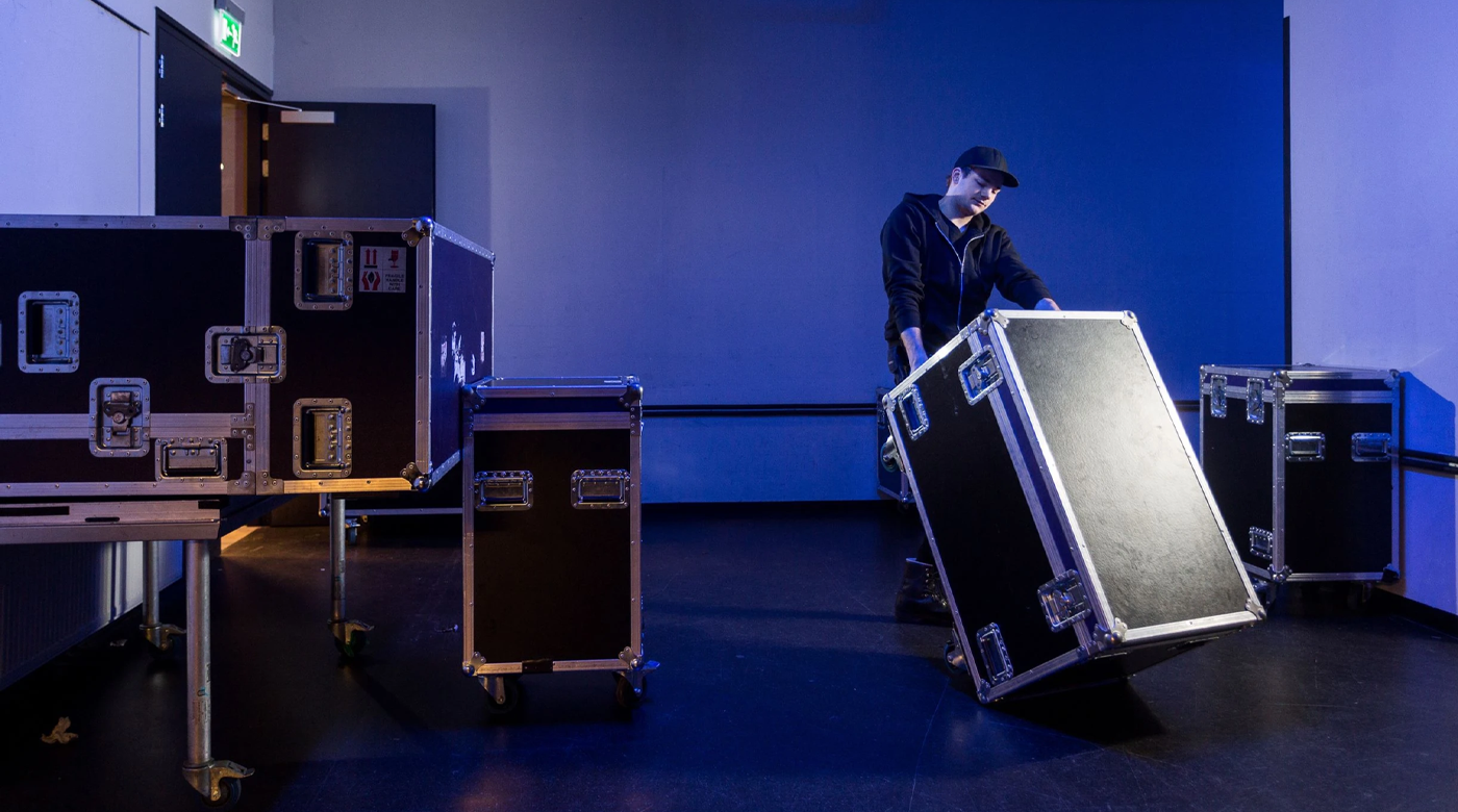 Equipe de produção movimentando cases e equipamentos, representando contratação e operação de fornecedores em eventos.